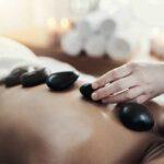 therapist placing a basalt stone on a woman's back, during a hot stone massage