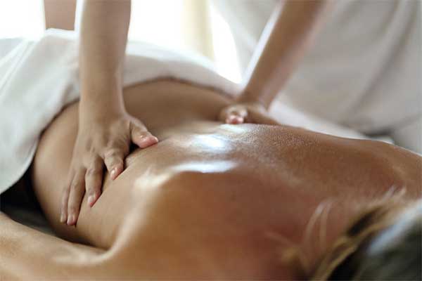 therapist applying massage techniques to a woman's back, during a Thai oil massage